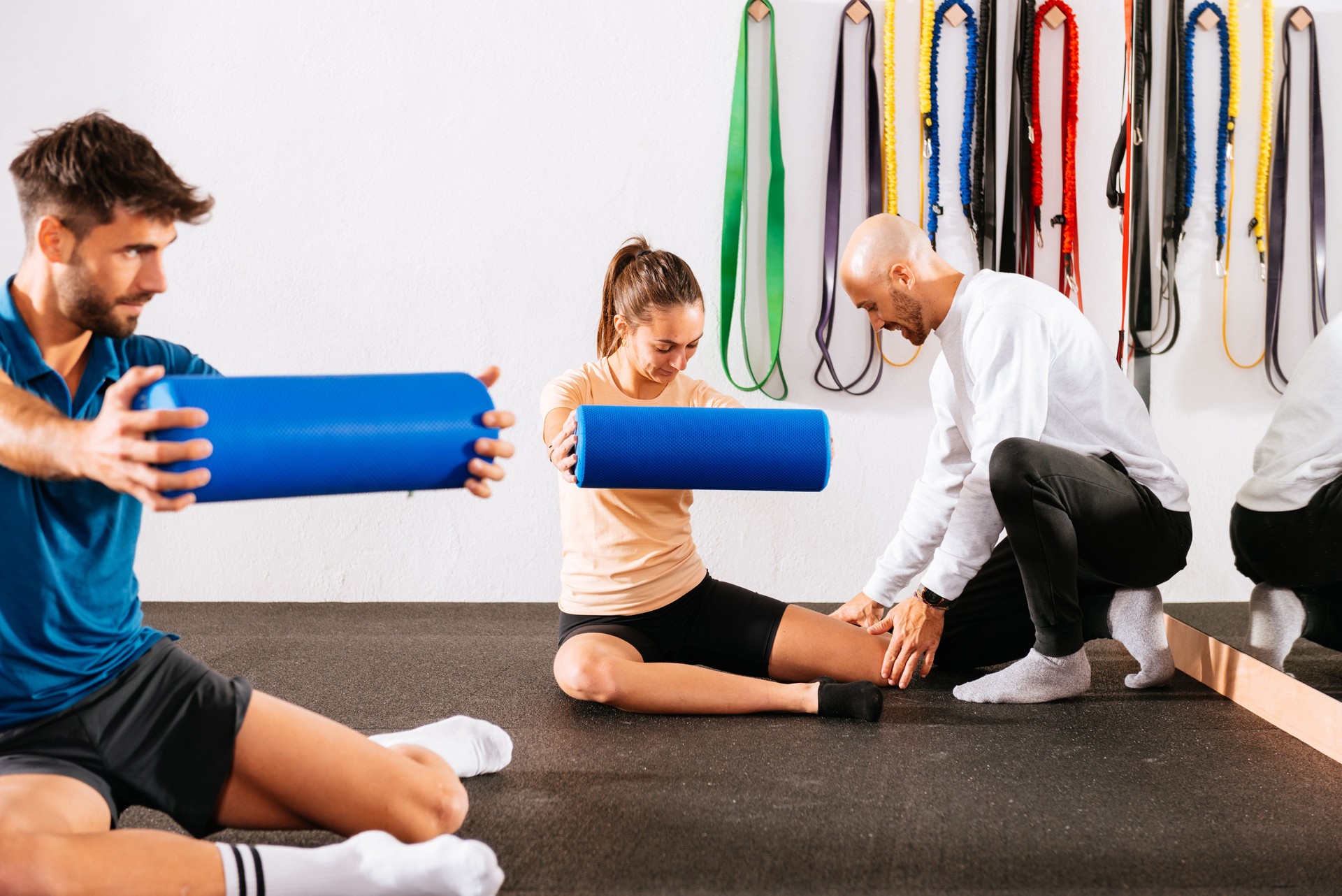 Trainer helping woman doing exercise with foam roller